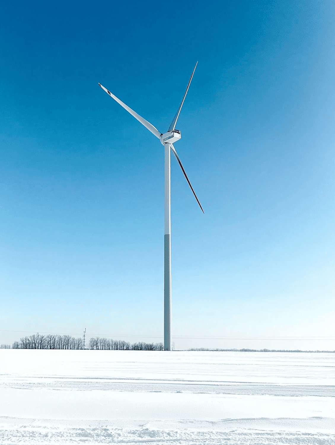 A single wind turbine standing in a snowy field under a clear blue sky